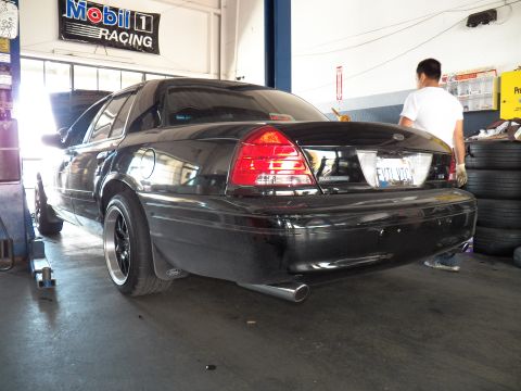 2003 Ford Crown Victoria - Black Crown Victoria from the left rear, technician working at the front of the bay