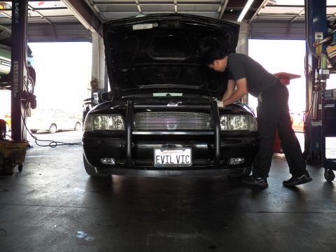 2003 Ford Crown Victoria - Mechanic works under the open hood of a black Crown Victoria with front brush guard