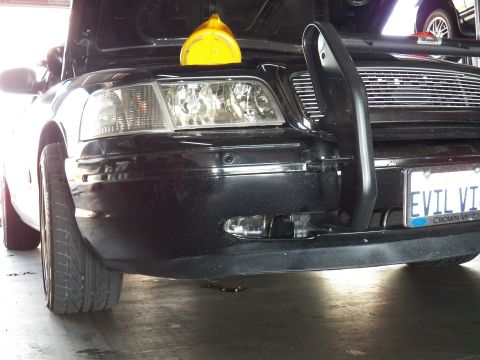 2003 Ford Crown Victoria - Detail of a black Crown Victoria's left headlight, push bar and front wheel from below