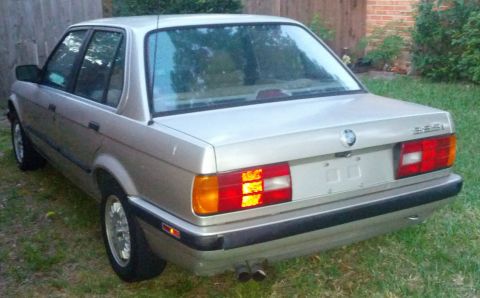 1989 BMW 3 Series - This 1989 BMW 325i sedan is shown from the rear, parked on a grassy area next to a wooden fence.
