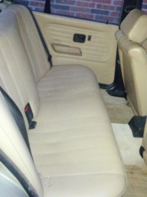 1989 BMW 3 Series - The interior of a vehicle shows a beige rear seat and door panel, with a brick wall visible in the background.