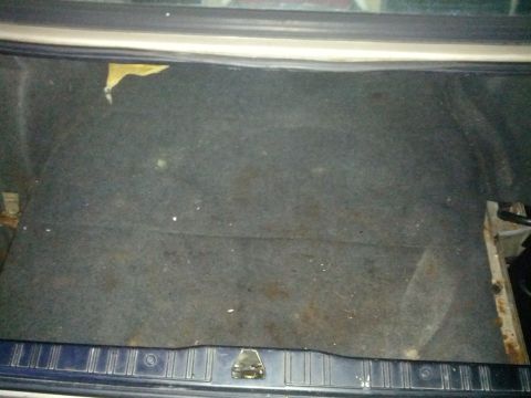 1989 BMW 3 Series - The interior of a car's trunk is shown, dark carpeting and a latch mechanism.