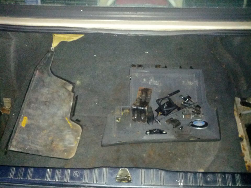 Car trunk interior with disassembled plastic trim and metal components scattered on the floor