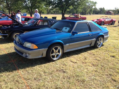1990 Ford Mustang - A blue 1990 Ford Mustang is displayed outdoors with other vehicles.