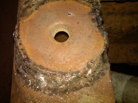 1986 Ford Bronco - Rusted metal bracket with a hole, showing signs of welding and corrosion.