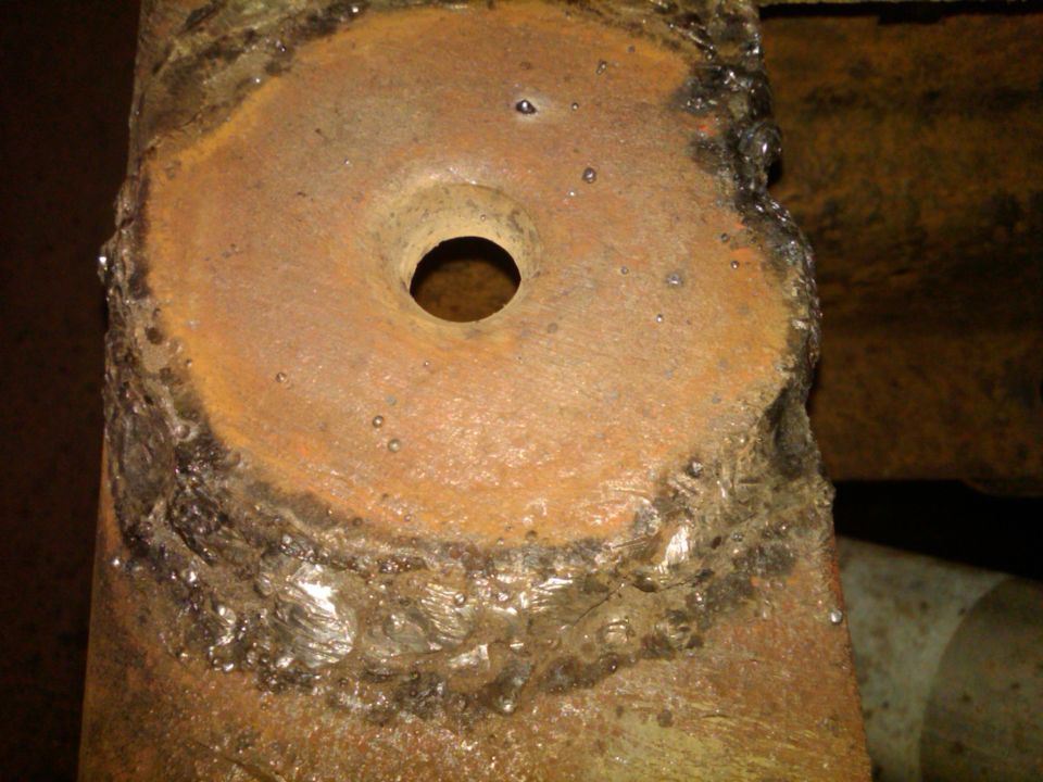 Close-up of a heavily rusted metal bracket with a central hole and visible weld marks