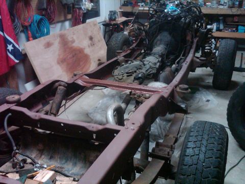 1986 Ford Bronco - This vehicle frame, engine, and transmission are in a garage, suggesting a rebuild or restoration project is underway.