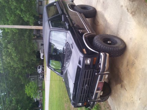 1986 Ford Bronco - This black Ford Bronco is parked on a concrete driveway with trees and houses in the background.