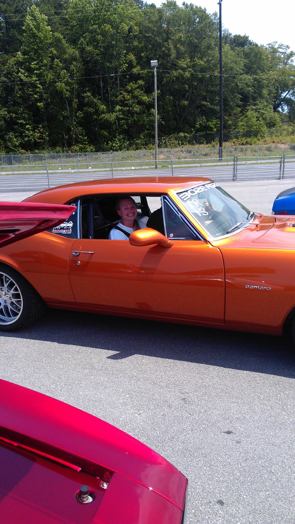 Orange 1969 Camaro with a person in the driver's seat, another red car in the foreground