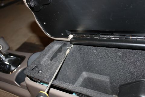 2003 Ford Crown Victoria - A screwdriver is used to pry open the center console compartment of a vehicle interior.