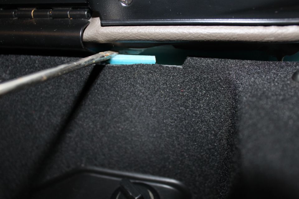 Screwdriver prying blue foam insulation inside car interior