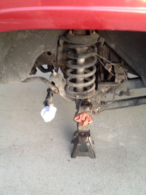 1997 Dodge 2500 - The front suspension of a vehicle is shown supported by jack stands, with a red body panel visible overhead.