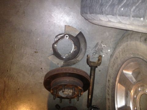1997 Dodge 2500 - Disassembled brake components, including a rotor and dust shield, lie on a concrete surface next to a tire.