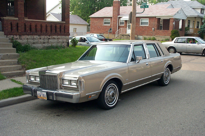Gold Lincoln Town Car sedan with wire wheels parked on residential street, yellow plate
