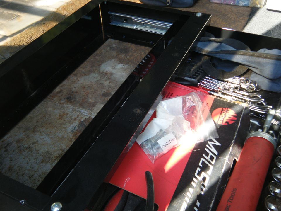 Open drawer of a black tool chest with various tools inside, including wrenches and a grease gun