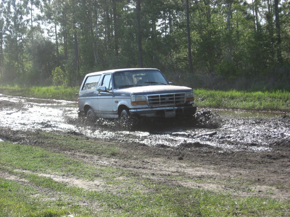 Ford Bronco driving through a muddy track with trees in the background