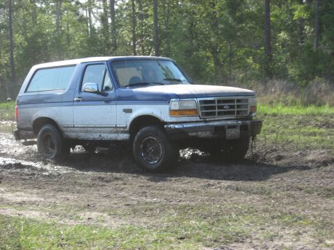 1994 Ford Bronco - This Ford Bronco is navigating a muddy off-road course with trees in the background.
