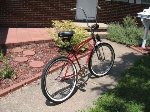 1994 Ford Bronco - A red cruiser bicycle with whitewall tires and tall handlebars is parked on a sidewalk in front of a brick house.