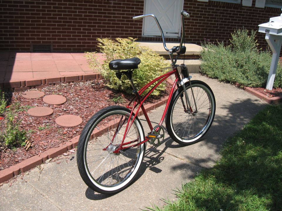 red cruiser bicycle with tall handlebars parked on a sidewalk