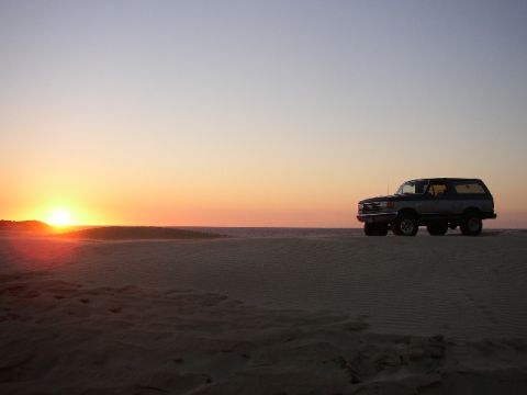 1989 Ford Bronco - A 1987 Ford Bronco sits on a sand dune as the sun sets over the horizon.