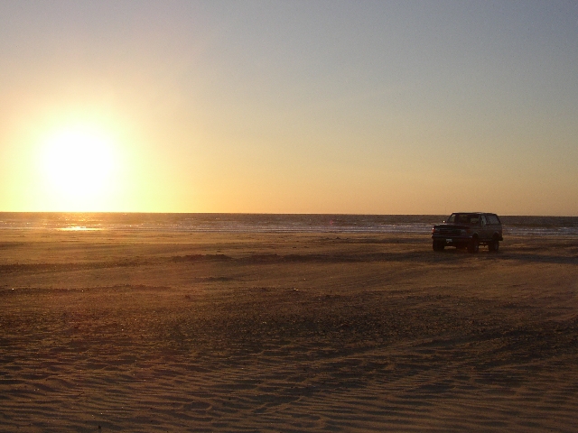 Dark full-size SUV parked on a sandy beach at sunset near the surf