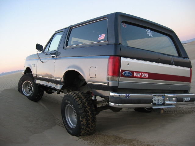 Lifted two-tone gray Ford Bronco, rear view, on sand dunes at dusk