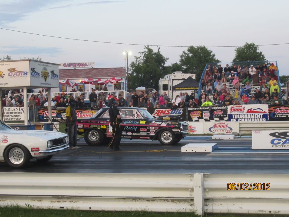 Two drag cars are lined up on a track with spectators in the background