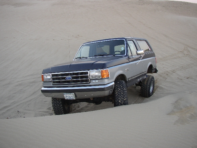 Two-tone gray Ford Bronco SUV lifted on large tires parked on sand dunes