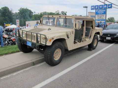 1991 Ford LTD Crown Victoria - tan open-door military Humvee parked at a curb at a car show, with a Metro Collision Center sign and motorcycles in the background.