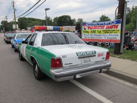 1991 Ford LTD Crown Victoria - green-and-white Ford Sheriff sedan number 351 leads a line of cars on a road beside a Special Olympics Torch Run banner.