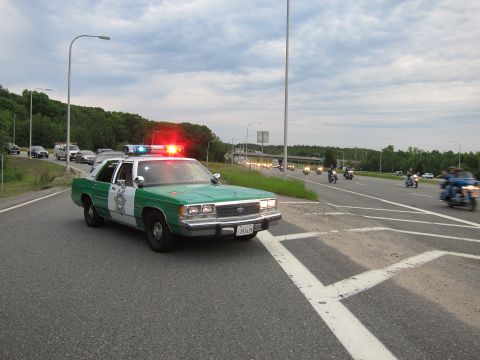 1991 Ford LTD Crown Victoria - green-and-white Ford Sheriff cruiser flashing red lights on a highway while a procession of motorcycles passes under an overpass.