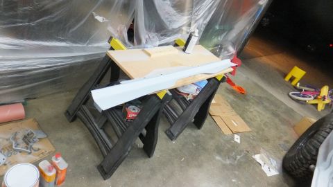 1983 Ford Bronco - A gray body panel is prepped on sawhorses, surrounded by tools and protective sheeting, suggesting ongoing automotive work.