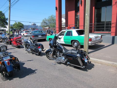 1991 Ford LTD Crown Victoria - Several motorcycles, including a black bagger, are parked at a curb in front of a green-and-white sheriff car beside a red-painted building.