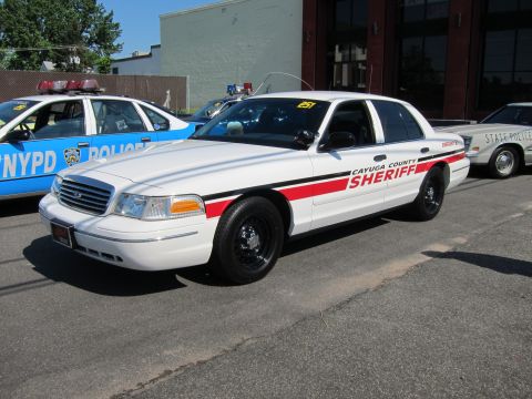 1991 Ford LTD Crown Victoria - white Ford Crown Victoria lettered Cayuga County Sheriff with a red stripe is parked next to a blue NYPD patrol car in a lot.