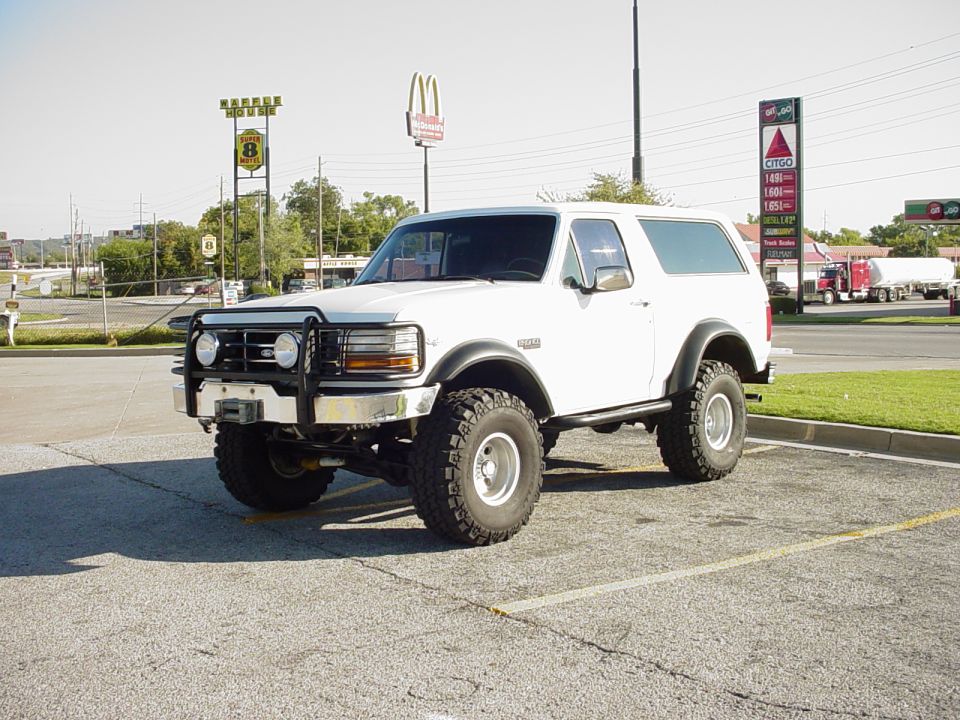 White lifted Ford full-size Bronco with brush guard parked in lot near gas station and McDonald's