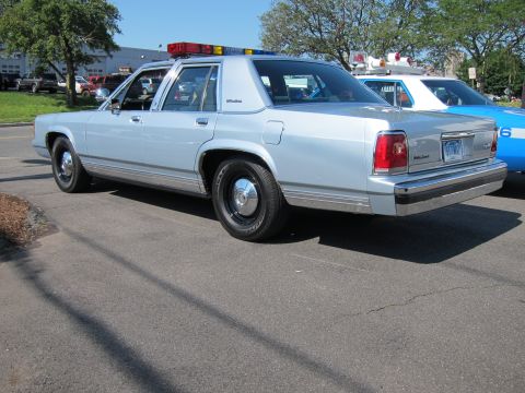 1991 Ford LTD Crown Victoria - silver Ford LTD Crown Victoria police sedan with a roof lightbar parked on pavement beside other cars at an outdoor gathering.