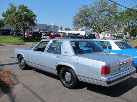 1991 Ford LTD Crown Victoria - silver Ford LTD Crown Victoria police sedan with red and blue roof lights sits in a lot with vehicles and trees behind it.