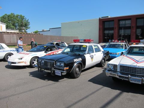 1991 Ford LTD Crown Victoria - black-and-white police sedan with a front push bar parked among several classic police cars at an outdoor show.
