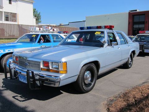 1991 Ford LTD Crown Victoria - silver Ford LTD Crown Victoria police sedan with a roof lightbar parked among other police cars at an outdoor event.