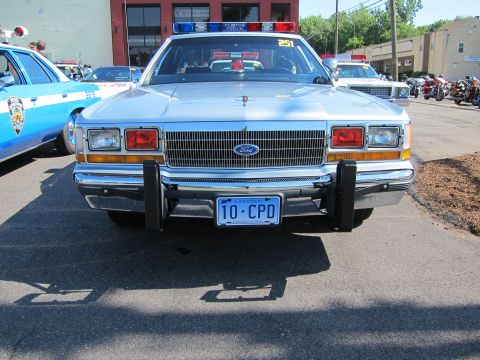 1991 Ford LTD Crown Victoria - Front view of a silver Ford LTD Crown Victoria police car with push bumpers and a '10-CPD' license plate among other cruisers.