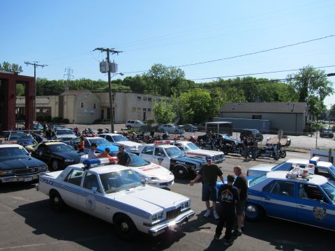 1991 Ford LTD Crown Victoria - Elevated view of numerous police cruisers and motorcycles parked in a lot with attendees standing among the vehicles.