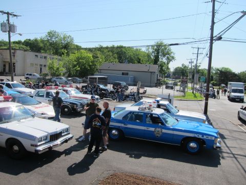 1991 Ford LTD Crown Victoria - Elevated view of a blue 'Police' sedan and other cruisers parked among people, motorcycles, and trees in a lot.