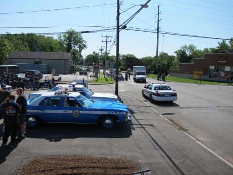 1991 Ford LTD Crown Victoria - blue-and-white police sedan with a roof lightbar parked near a road as a white Crown Victoria cruiser sits across the way.
