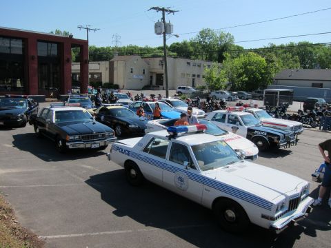 1991 Ford LTD Crown Victoria - white police sedan bearing a city seal parked among classic police cars and motorcycles at an outdoor gathering.