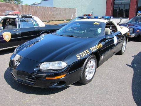 1991 Ford LTD Crown Victoria - black Chevrolet Camaro marked 'State Trooper' with a roof lightbar parked among other police cars at an outdoor show.