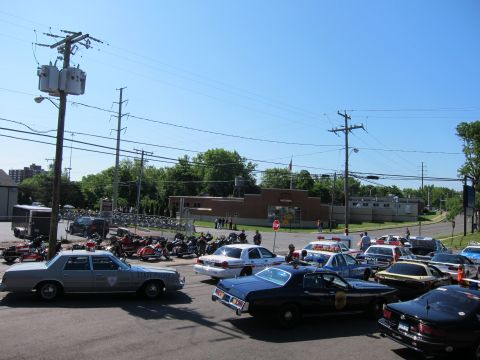 1991 Ford LTD Crown Victoria - Elevated view of a parking lot crowded with police cruisers and motorcycles beneath utility poles and a clear blue sky.