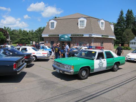 1991 Ford LTD Crown Victoria - green-and-white police sedan parks with other cruisers outside the brick Modugno Electric building.