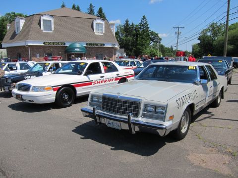 1991 Ford LTD Crown Victoria - white sedan marked State Police and a red-striped Sheriff cruiser parked outside a brick building.