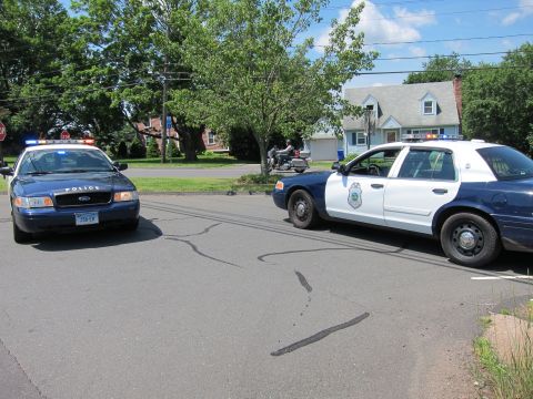 1991 Ford LTD Crown Victoria - Two blue police cruisers parked across a residential street with a motorcycle visible in the background.