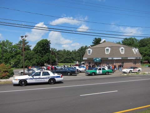 1991 Ford LTD Crown Victoria - lineup of police cruisers and classic cars parked outside a brick building as a small crowd gathers.